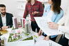 a group of people working around a model of a residential complex with building plans